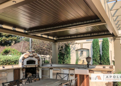 Apollo louver system integrated into custom framing and columns over a beautiful outdoor cooking and dining area.