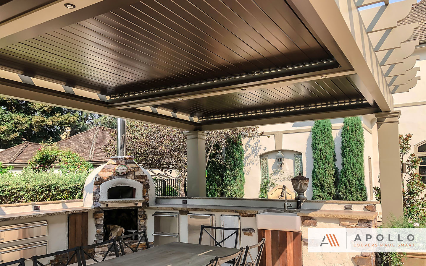 Apollo louver system integrated into custom framing and columns over a beautiful outdoor cooking and dining area.