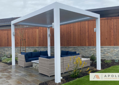 Freestanding all-white louvered roof over a small backyard seating area, providing shade and comfort for outdoor relaxation.