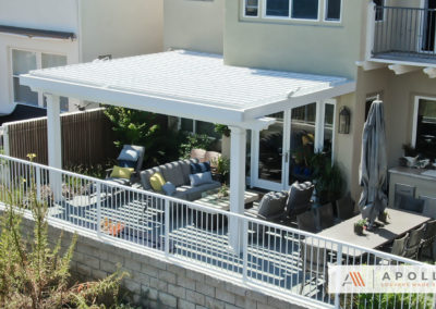 White louvered pergola attached to wall providing shelter over outdoor seating area