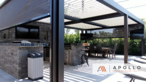 Louvered roof over an outdoor cooking, dining, and entertaining area featuring drop screens and outdoor TVs.