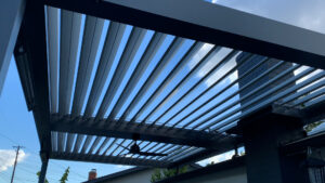 Louvered pergola with roof attachment - partially open, revealing blue sky with a few clouds