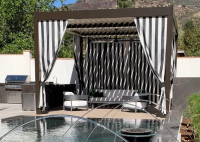 Personalized pergola design featuring striped curtains stands poolside creating unique outdoor space.