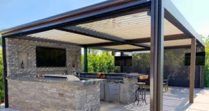 Freestanding louvered roof pergola with outdoor kitchen and entertainment area in homeowner's backyard.