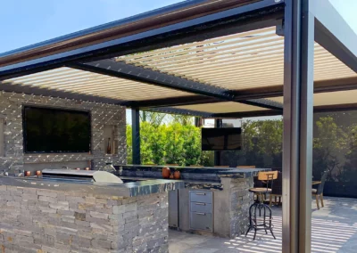 Freestanding louvered roof pergola with outdoor kitchen and entertainment area in homeowner's backyard.