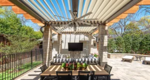 Custom adjustable louvered pergola with integrated fan provides shading over homeowner's outdoor entertainment area.