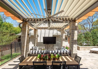 Custom adjustable louvered pergola with integrated fan provides shading over homeowner's outdoor entertainment area.