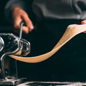 Hand-operated pasta maker rolling out thin dough, symbolizing the roll forming process of aluminum.
