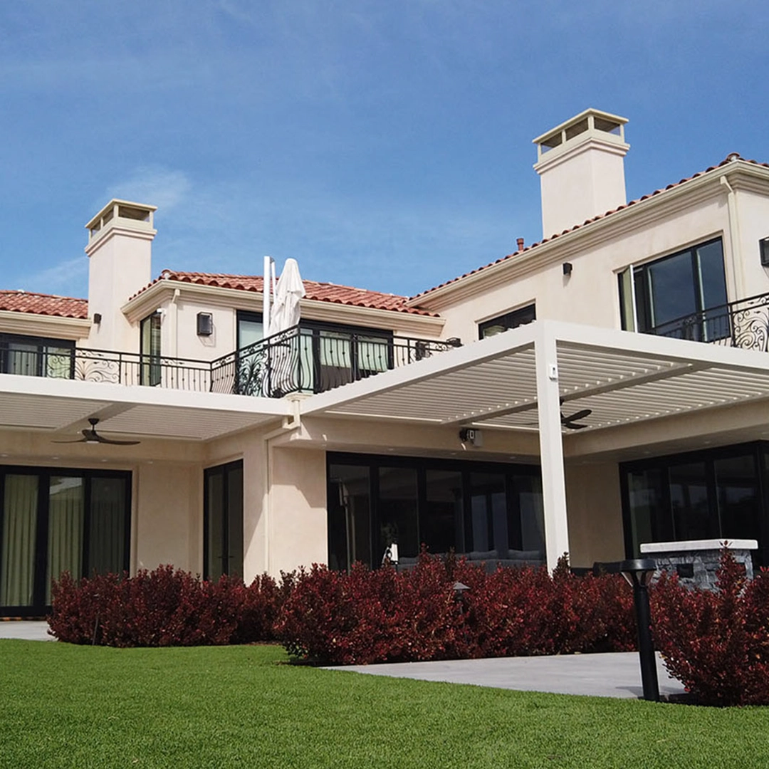 Mediterranean-style home with terracotta roof tiles and a white louvered pergola in the foreground.