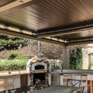 Outdoor pergola with smart Apollo louvers over an outdoor cooking and dining area featuring a stone pizza oven.