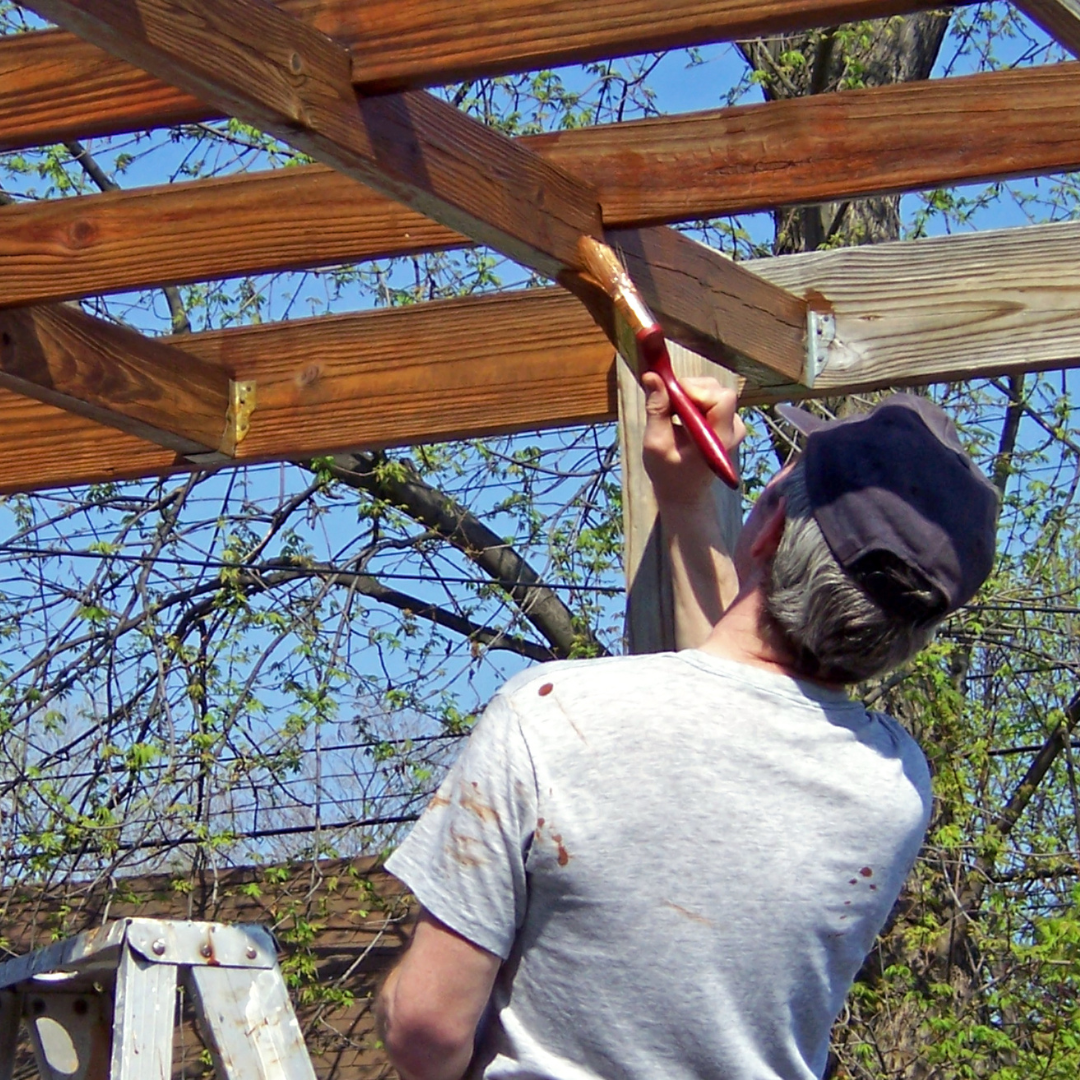 Man applying wood stain to a pergola to enhance durability and appearance.