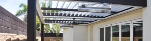 Open louvers of an Apollo pergola casting a geometric shadow on a stylish outdoor lounge area.