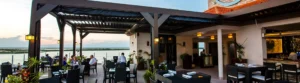 Waterfront dining under Apollo's elegant louvered pergola at dusk.