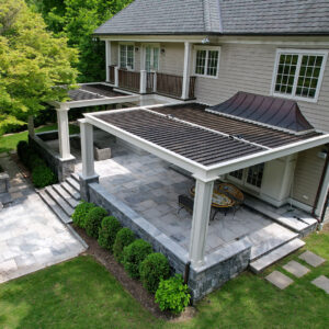 Elevated stone patio with two white louvered pergolas and outdoor dining area