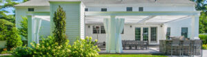 White pergola with curtains over backyard patio dining and grill area
