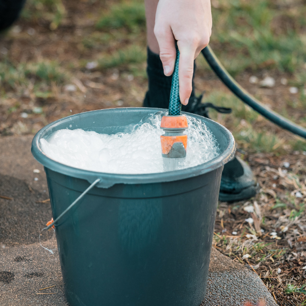 Person filling gray bucket with soapy water using garden hose