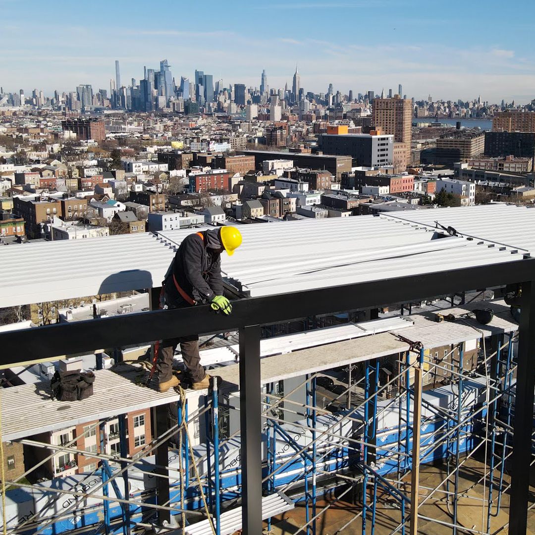 Construction worker installing louvered pergola on rooftop with city skyline