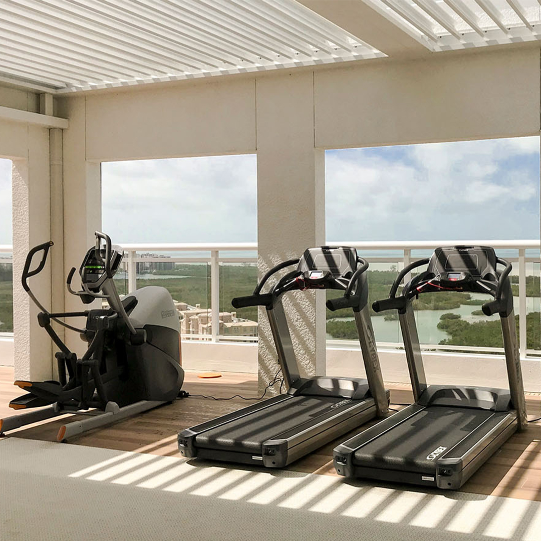 Covered rooftop gym with treadmills under a louvered pergola