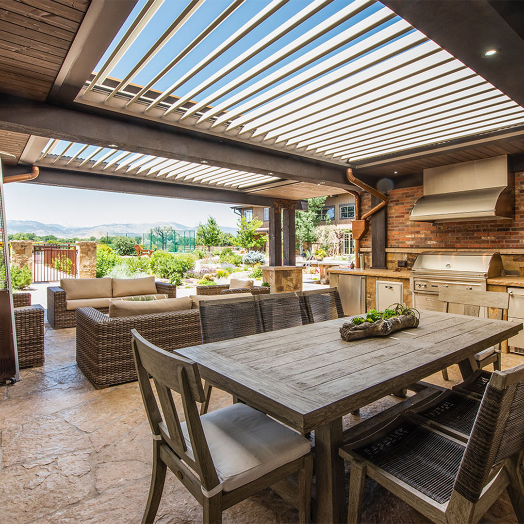 Outdoor kitchen and dining area beneath a louvered pergola