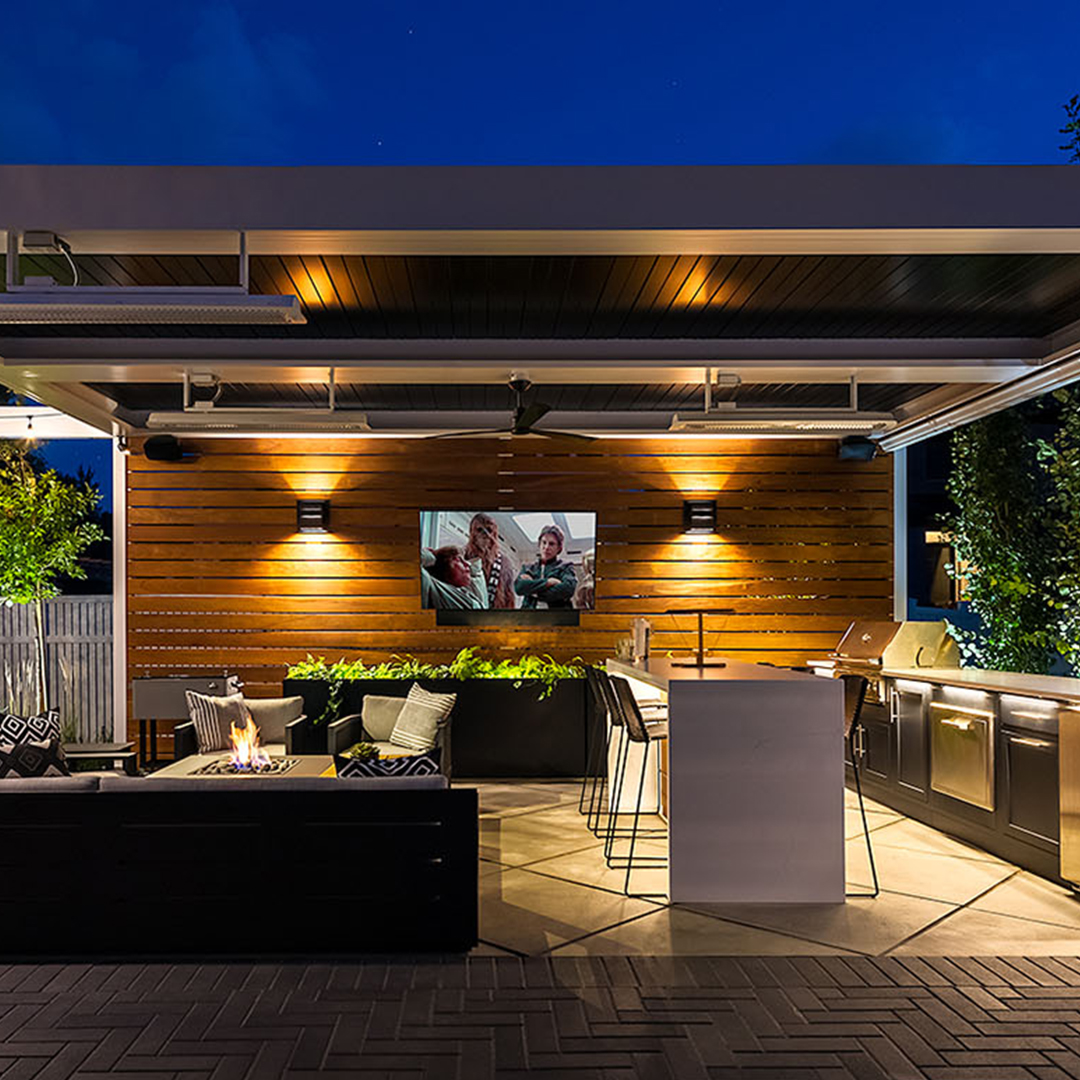 Modern outdoor living pavilion with pergola, lighting, and fire feature at night