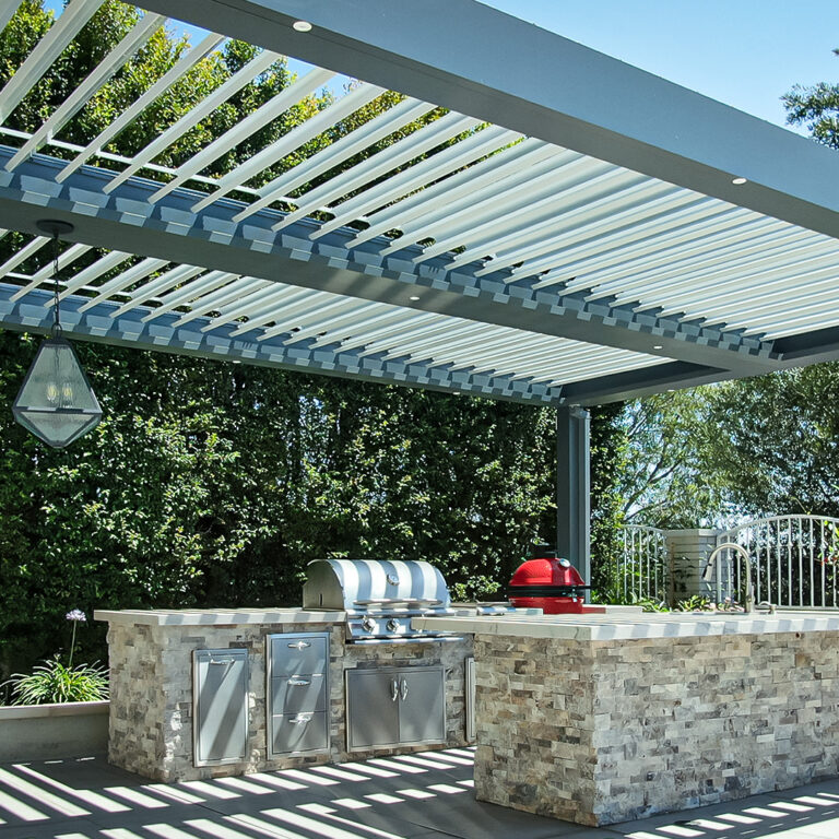 Wide view of outdoor kitchen beneath a two-bay freestanding louvered pergola