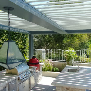 Sink and grill area beneath a freestanding pergola with open louvers