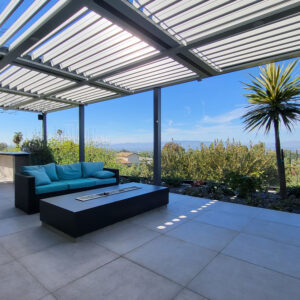 Modern wall-attached louvered pergola covering an outdoor seating area with sofa, fire table, mountain views, and filtered sunlight.