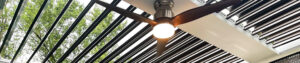 Ceiling fan mounted beneath bronze louvers on a wall-attached pergola
