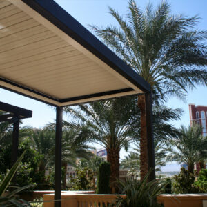 Dark-framed aluminum louvered pergola with closed louvers over a commercial rooftop terrace surrounded by palm trees and a city skyline