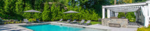 Panoramic poolside view of white louvered pergola and lounge chairs in Tenafly NJ