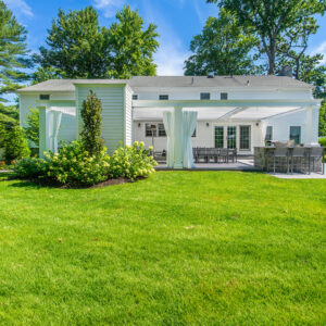 Rear exterior view of white wall-attached louvered pergola covering patio in Tenafly NJ