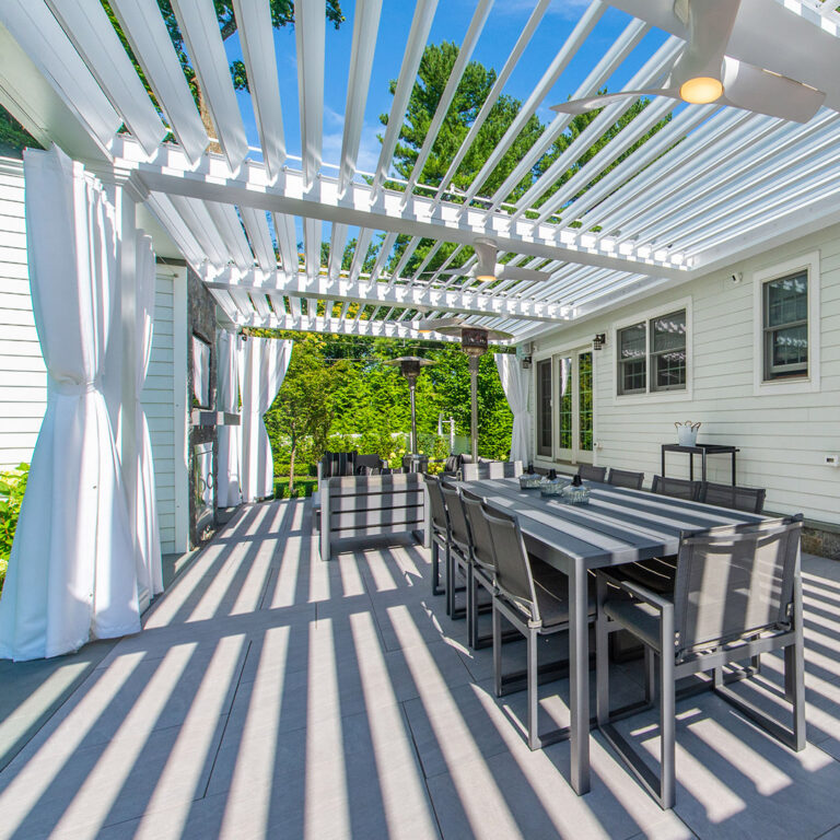Outdoor dining area beneath white louvered pergola with fans and curtains in Tenafly NJ