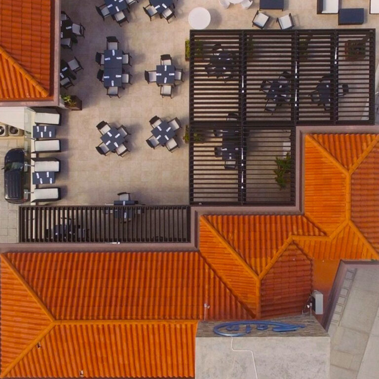 Drone shot looking down at a dark aluminum louvered pergola over an outdoor dining patio surrounded by terracotta rooftops