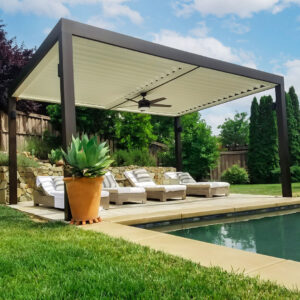Freestanding dark aluminum pergola with closed cream-colored louvers and a ceiling fan shading four chaise lounges beside a backyard pool
