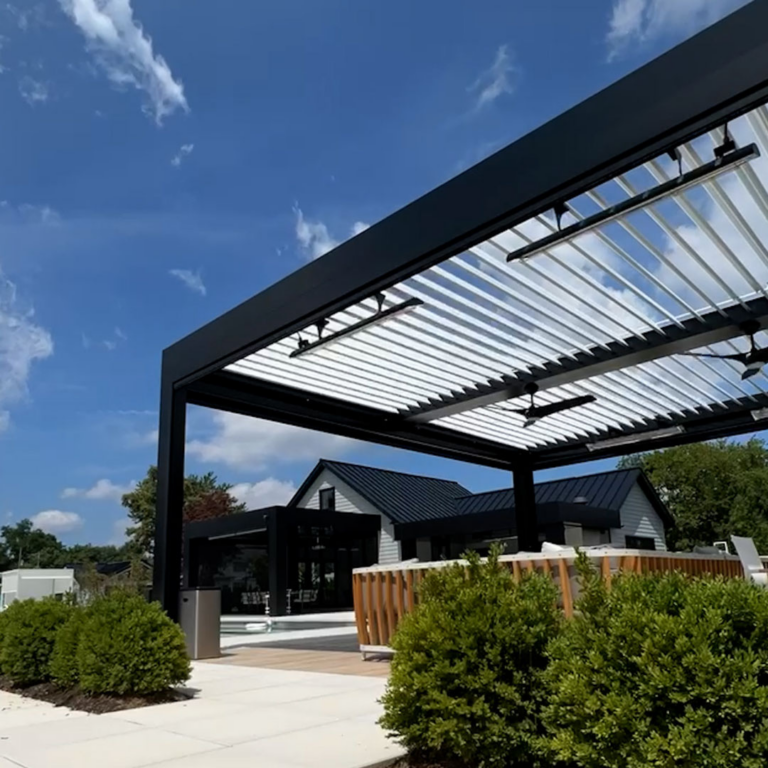 Large black aluminum louvered pergola with fully open louvers and two ceiling fans, installed beside a modern black and white home with cedar privacy screening