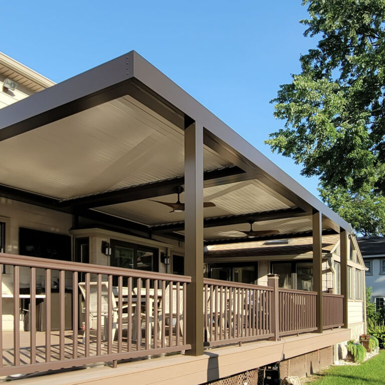 Large bronze aluminum louvered pergola with closed louvers and two ceiling fans covering a raised deck with railing attached to a suburban home