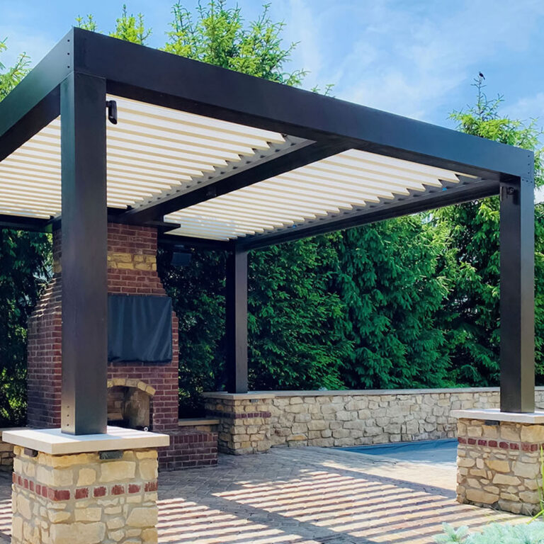 Freestanding dark-framed aluminum louvered pergola with open cream louvers beside a brick fireplace and outdoor TV on a paver patio with a pool in the background