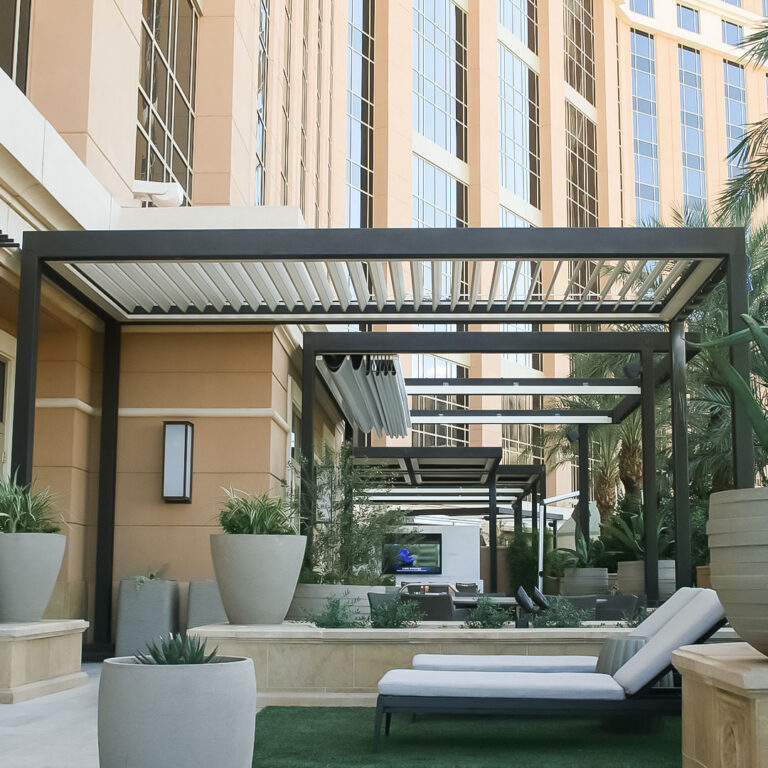 Dark aluminum louvered pergolas line a resort pool courtyard with chaise lounges, planters, and a high-rise hotel backdrop