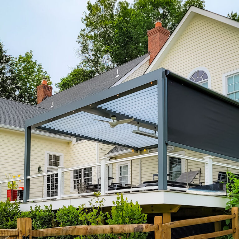 Dark aluminum louvered pergola with open louvers, a deployed motorized side screen, ceiling fan, and integrated LED lighting on an elevated residential deck