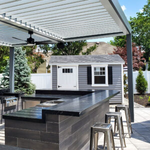 White aluminum louvered pergola with open louvers and a ceiling fan shading a dark stone outdoor kitchen bar with stainless bar stools and a built-in grill