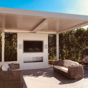 Cream aluminum louvered pergola with closed louvers, recessed speakers, and downlights over a wicker lounge facing a wall-mounted outdoor TV, flanking in-wall speakers, and a built-in linear fireplace