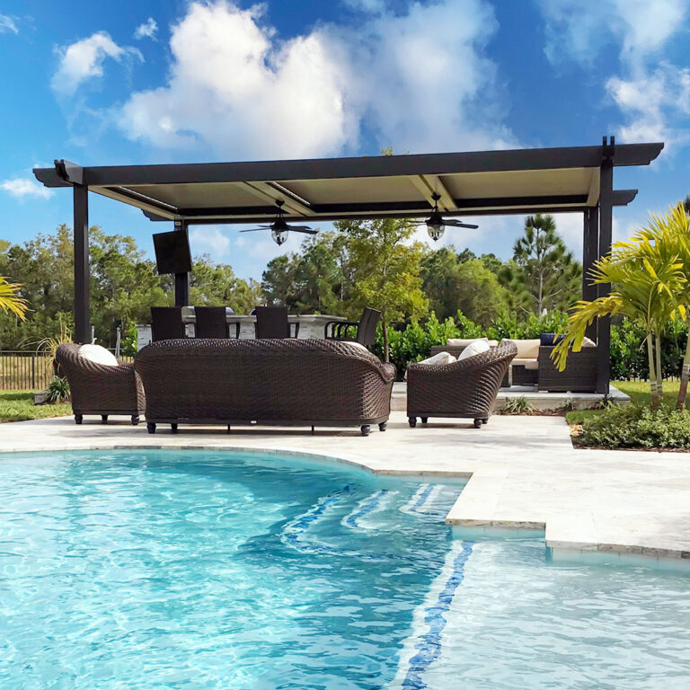 Dark aluminum motorized pergola with two ceiling fans shading a poolside seating area with wicker furniture and a freeform pool in the foreground