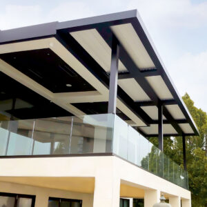 Large multi-bay dark aluminum louvered pergola with closed cream louvers, recessed lighting, and a cassette AC unit on an upper balcony of a luxury contemporary home with frameless glass railings