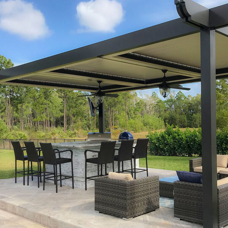 Large multi-bay dark aluminum louvered pergola with closed cream louvers and dual ceiling fans over an outdoor kitchen bar with marble surround, kamado grill, wicker lounge seating, and a Florida pine forest beyond