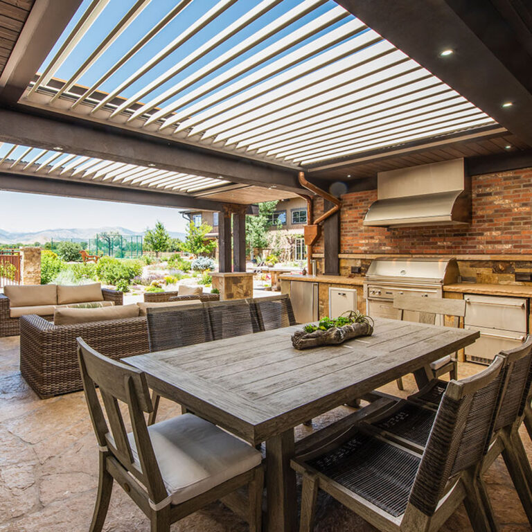 Open louvered roof above an outdoor kitchen and dining area with mountain views and recessed lighting
