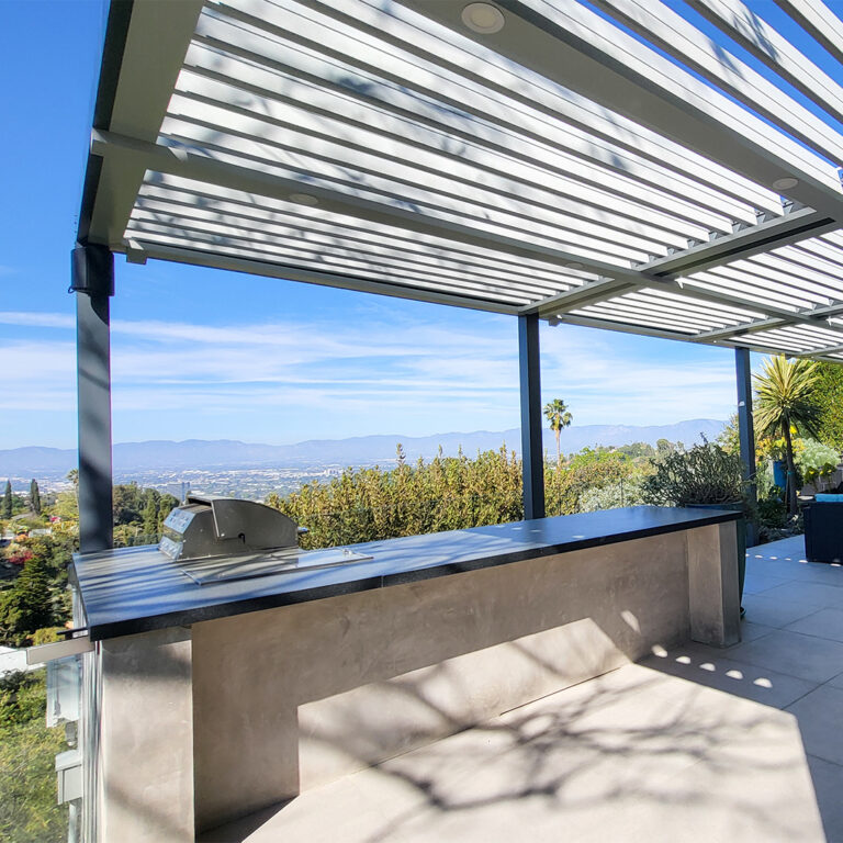 Aluminum louvered pergola shading a built-in outdoor kitchen with mountain and city views stretching to the horizon