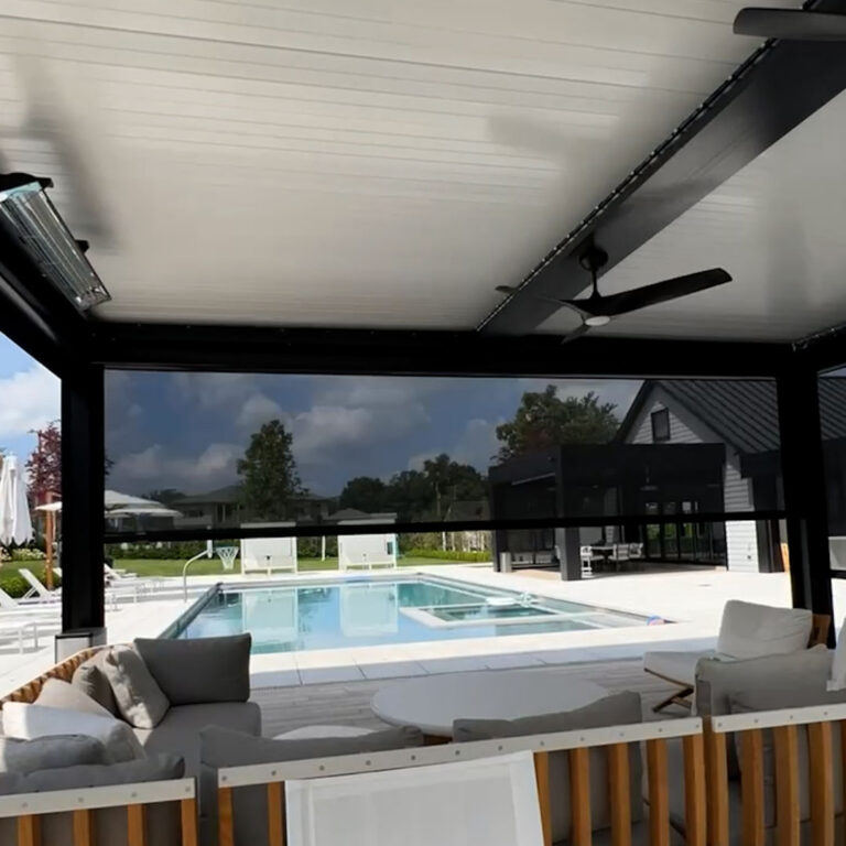 Interior view of a black aluminum louvered pergola with motorized screens deployed, a ceiling fan, and a radiant heater overlooking a backyard pool