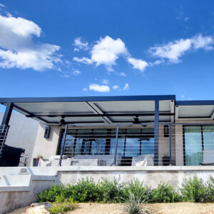 Dark aluminum louvered pergola with closed louvers and dual ceiling fans spanning a rooftop deck with glass railing on a modern home