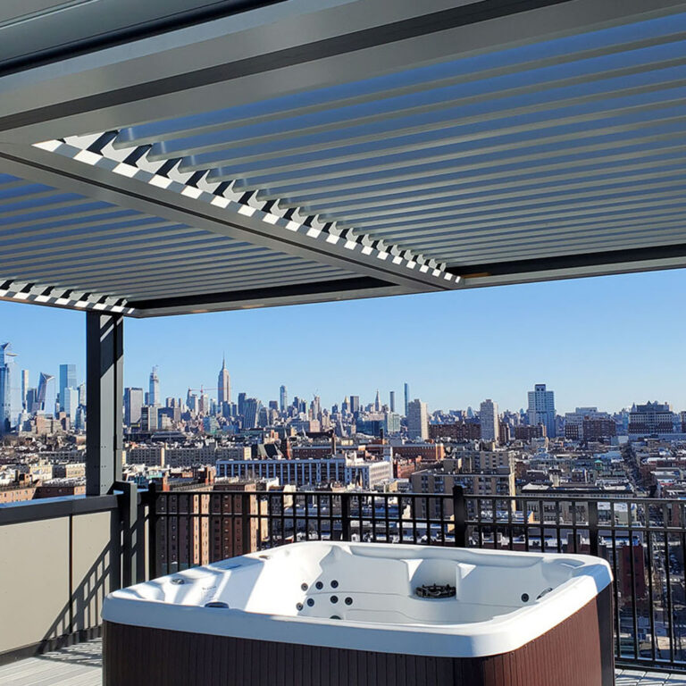 Aluminum louvered pergola with partially open louvers covering a rooftop hot tub, with a dense urban skyline including the Empire State Building visible beyond