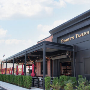 Large closed louvered pergola spanning the full front patio of Tommy's Tavern with mounted heaters, string lights, and dining tables inside